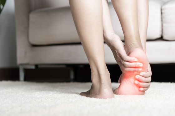 Person holding their painful heel with a glowing red area, indicating nerve pain or neuropathy symptoms in the foot.
